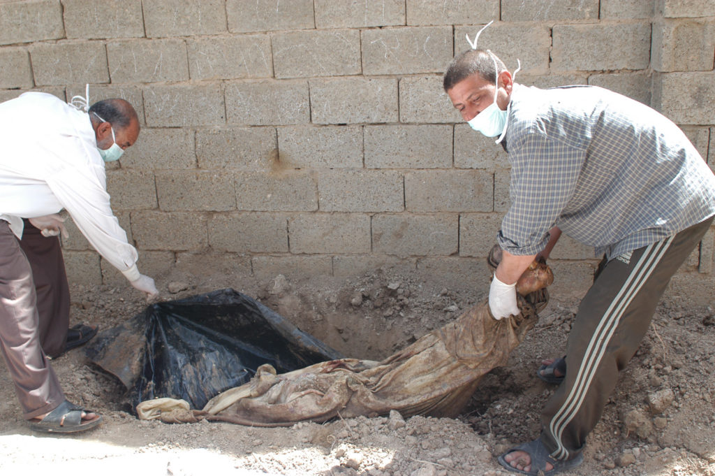 Iraqi volunteers in surgical masks pull a woman’s corpse out of the front yard of a Fallujah home, where she was temporarily buried.