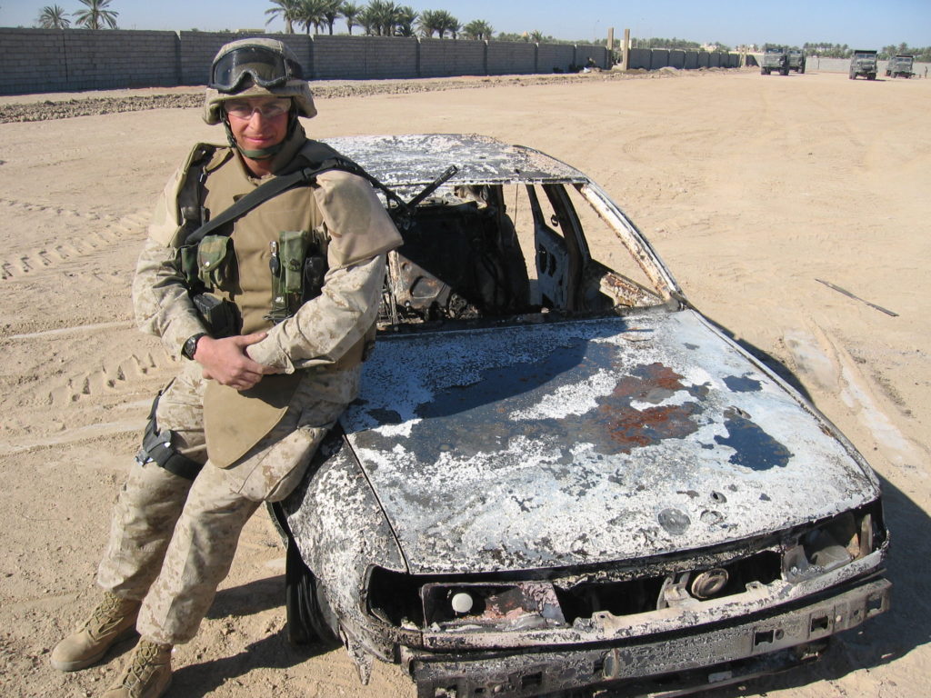 Marine Sgt. Adam Kokesh poses for a so-called trophy photo with a car that Marines shot up at a checkpoint, killing the Iraqi driver in the hail of machine-gun fire.